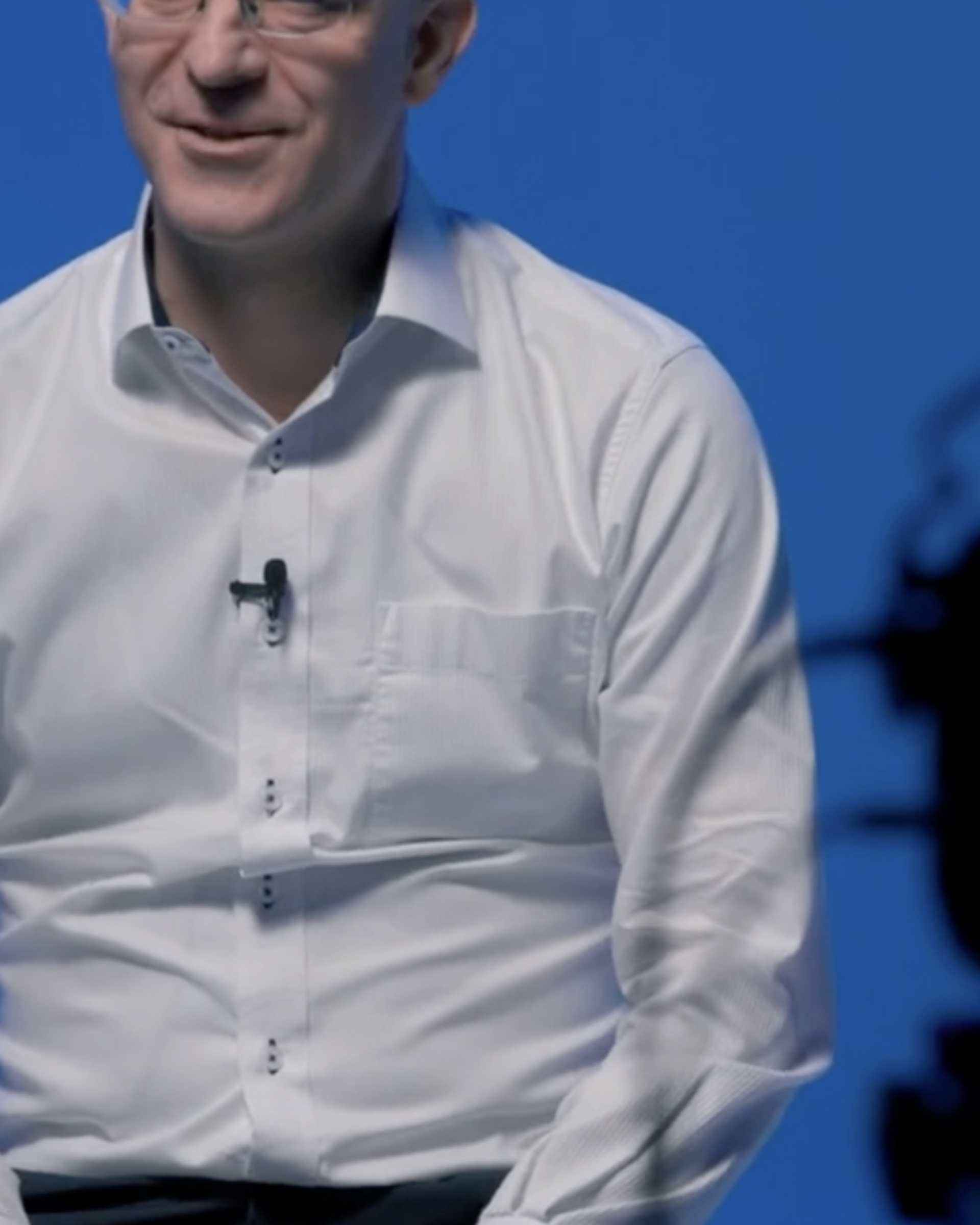 Notre CSO Erik Edelmann portant une chemise blanche est assis derrière une caméra. Il est en train d'être interviewé et l'interview est filmée