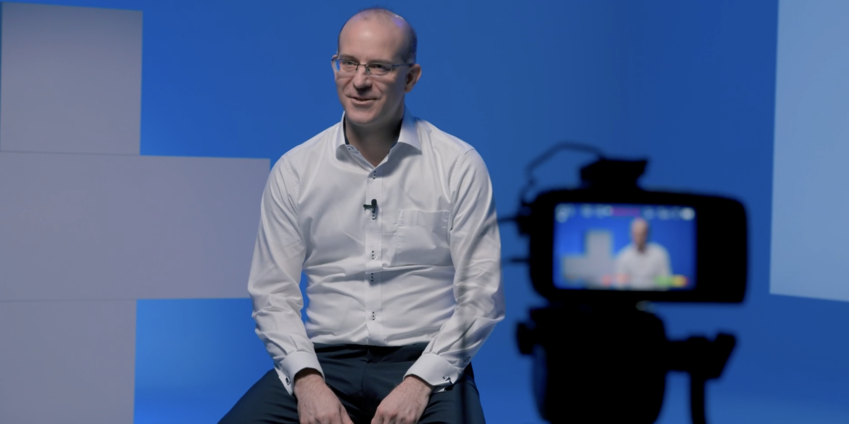 Notre CSO Erik Edelmann portant une chemise blanche est assis derrière une caméra. Il est en train d'être interviewé et l'interview est filmée
