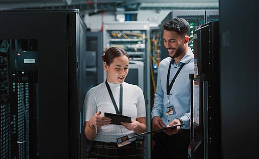 Two persons are standing in a server room discussing something 
