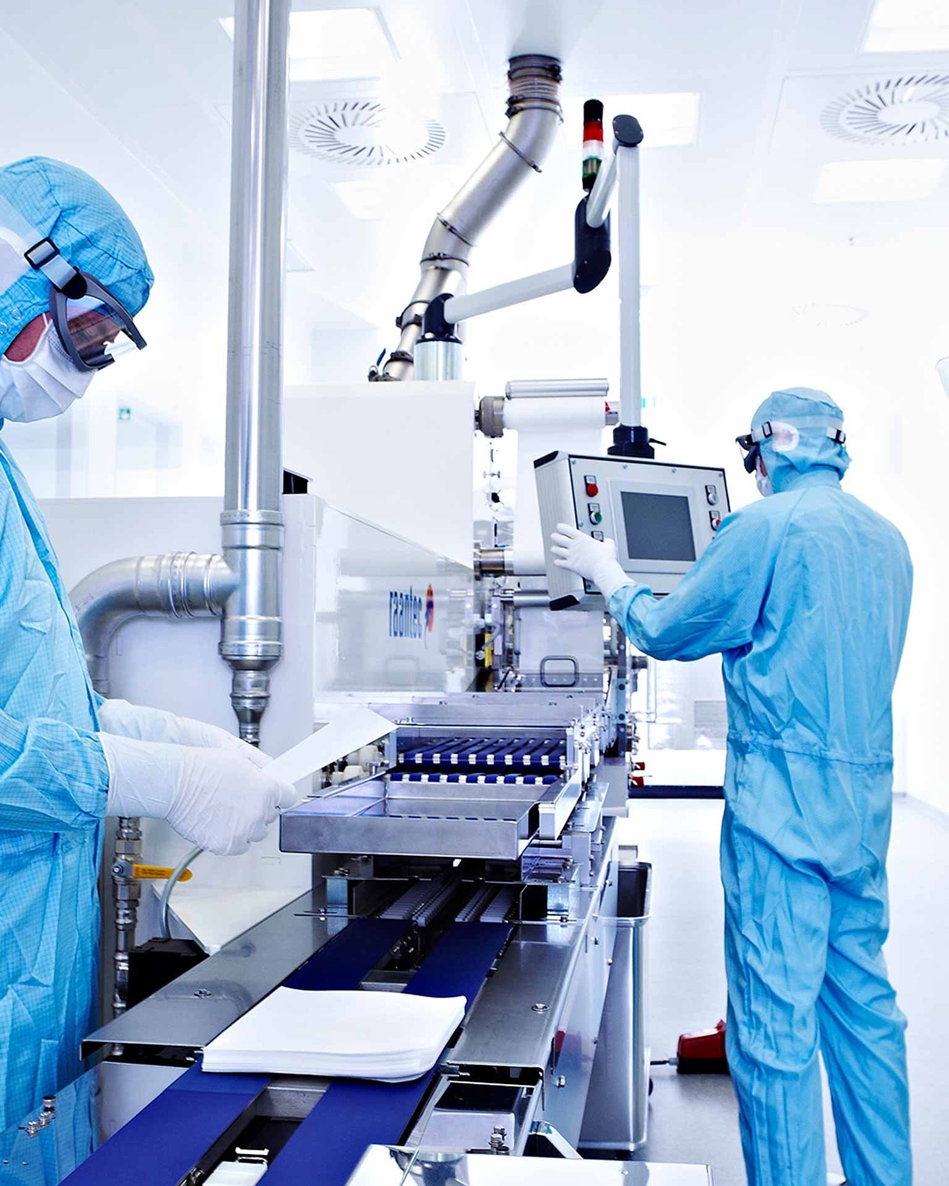 Zwei Personen in blauen Schutzanzügen und Masken arbeiten in einem sterilen Reinraum mit medizinischen Geräten