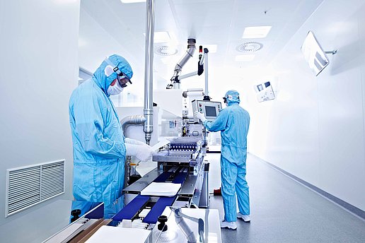 Zwei Personen in blauen Schutzanzügen und Masken arbeiten in einem sterilen Reinraum mit medizinischen Geräten