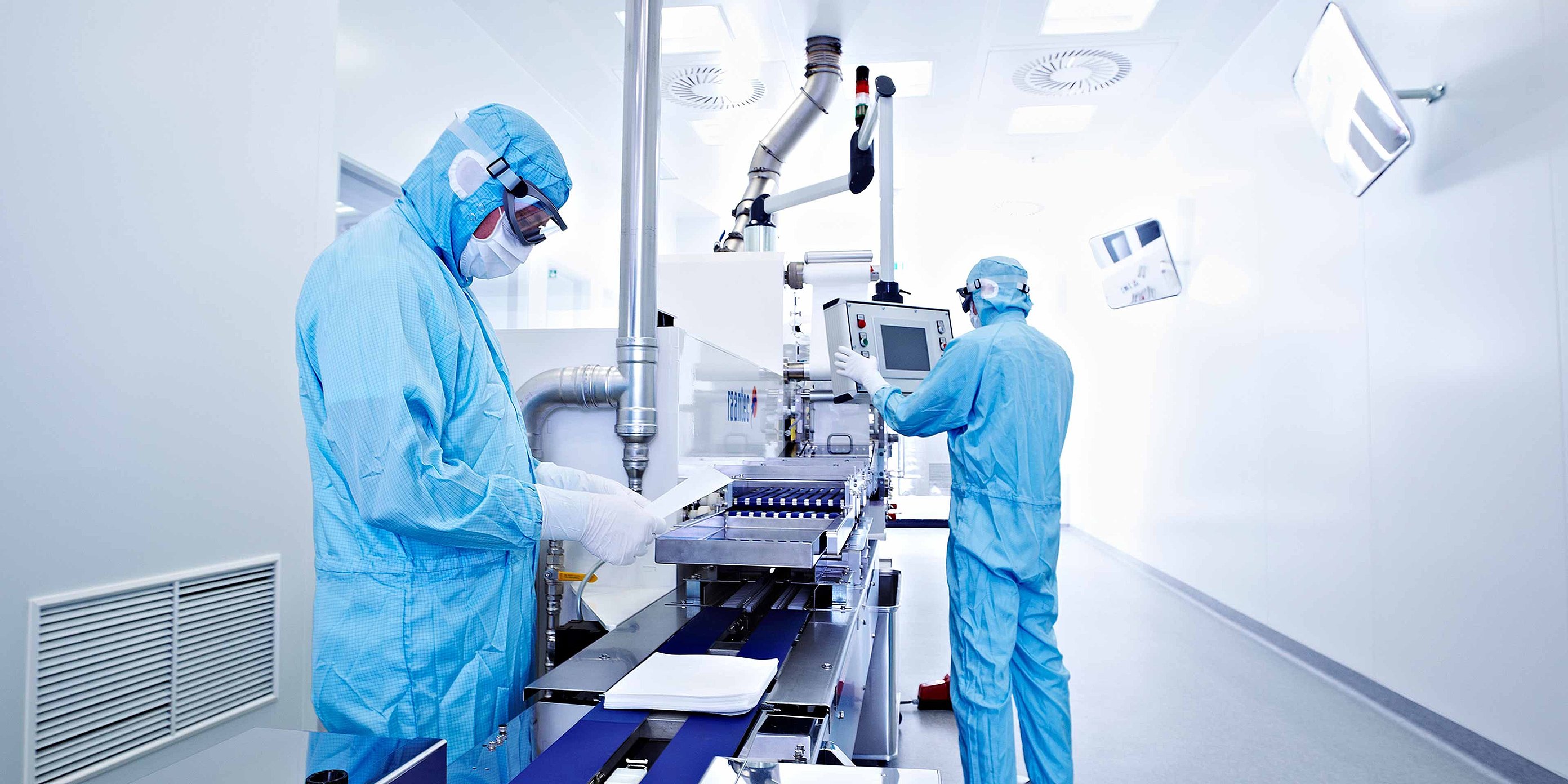 Two persons in in blue protective suits and masks are working in a sterile clean room with medical devices