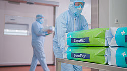Personen in Schutzanzügen in einem Reinraum, im Vordergrund Stapel mit SepaFlex®-Verpackungen