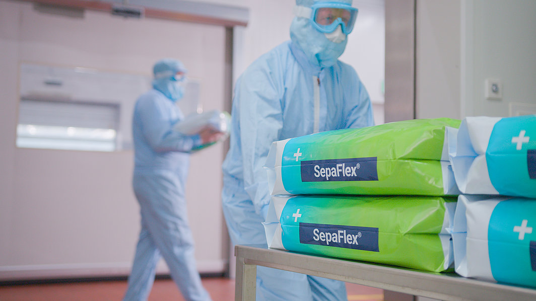 Personen in Schutzanzügen in einem Reinraum, im Vordergrund Stapel mit SepaFlex®-Verpackungen