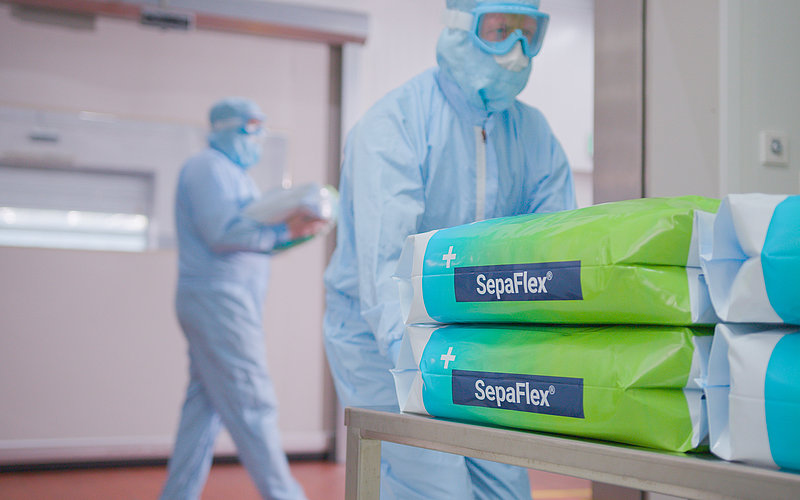 Personnes en combinaison de protection dans une salle blanche, au premier plan, pile d’emballages SepaFlex®