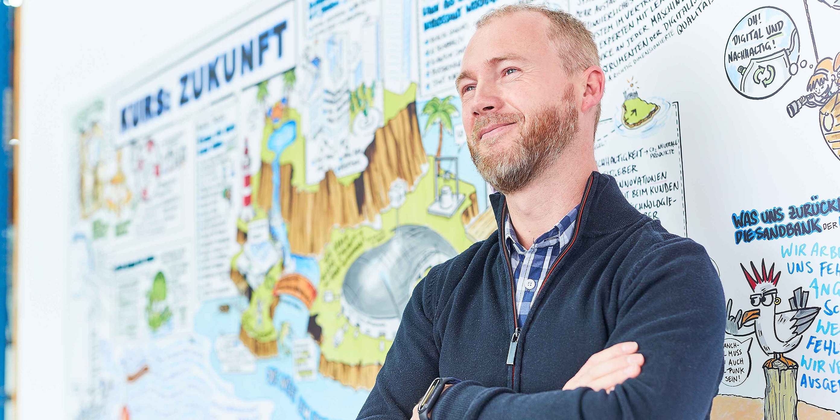 An employee is standing in front of a colorful wall. The values of Bischof+Klein can be seen painted as a blurred comic strip in the background.