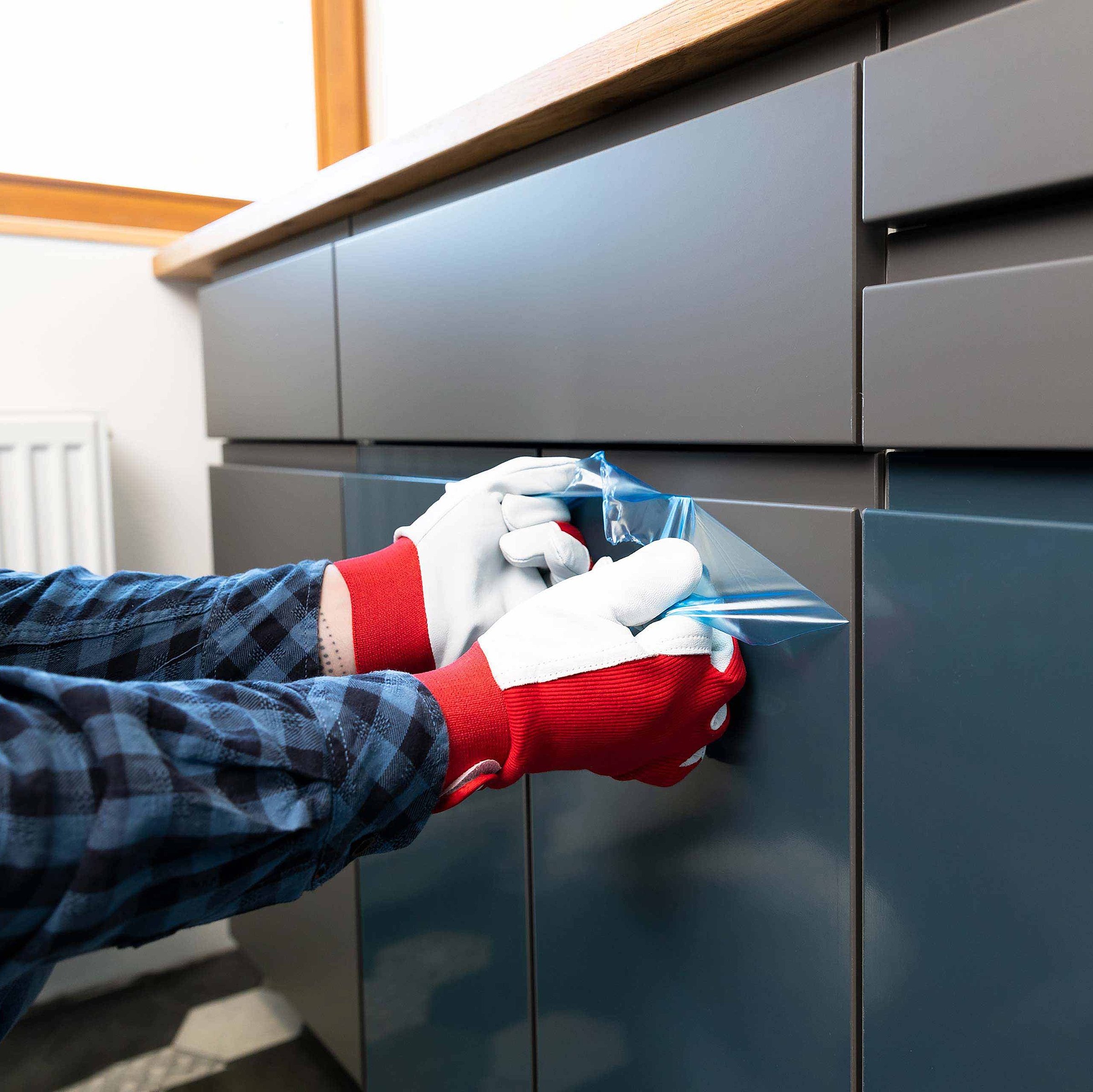 A person wearing white/red protective gloves is removing protective film from a gray kitchen front