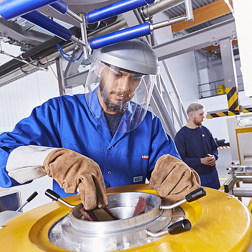 An employee wearing protective clothing, safety gloves, and safety goggles in the Innovation Center in Lengerich. He is standing at a line and conducting tests.