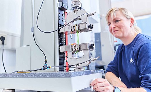 Eine Mitarbeiterin sitzt vor einem Mikroskop im Labor und prüft die Produkte auf ihre Vorgaben und Qualität
