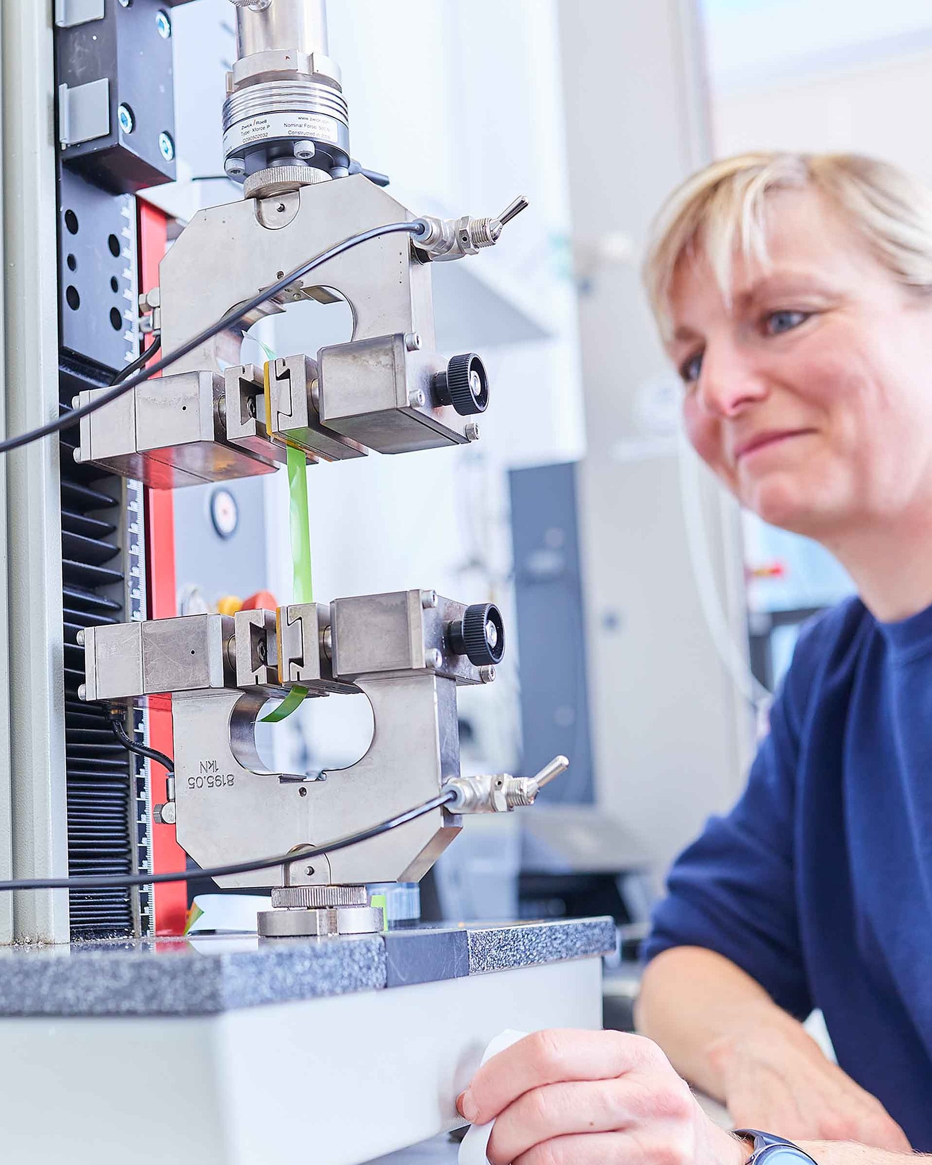 An employee is sat before a microscope in the laboratory and is checking the products for quality and adherence to specifications