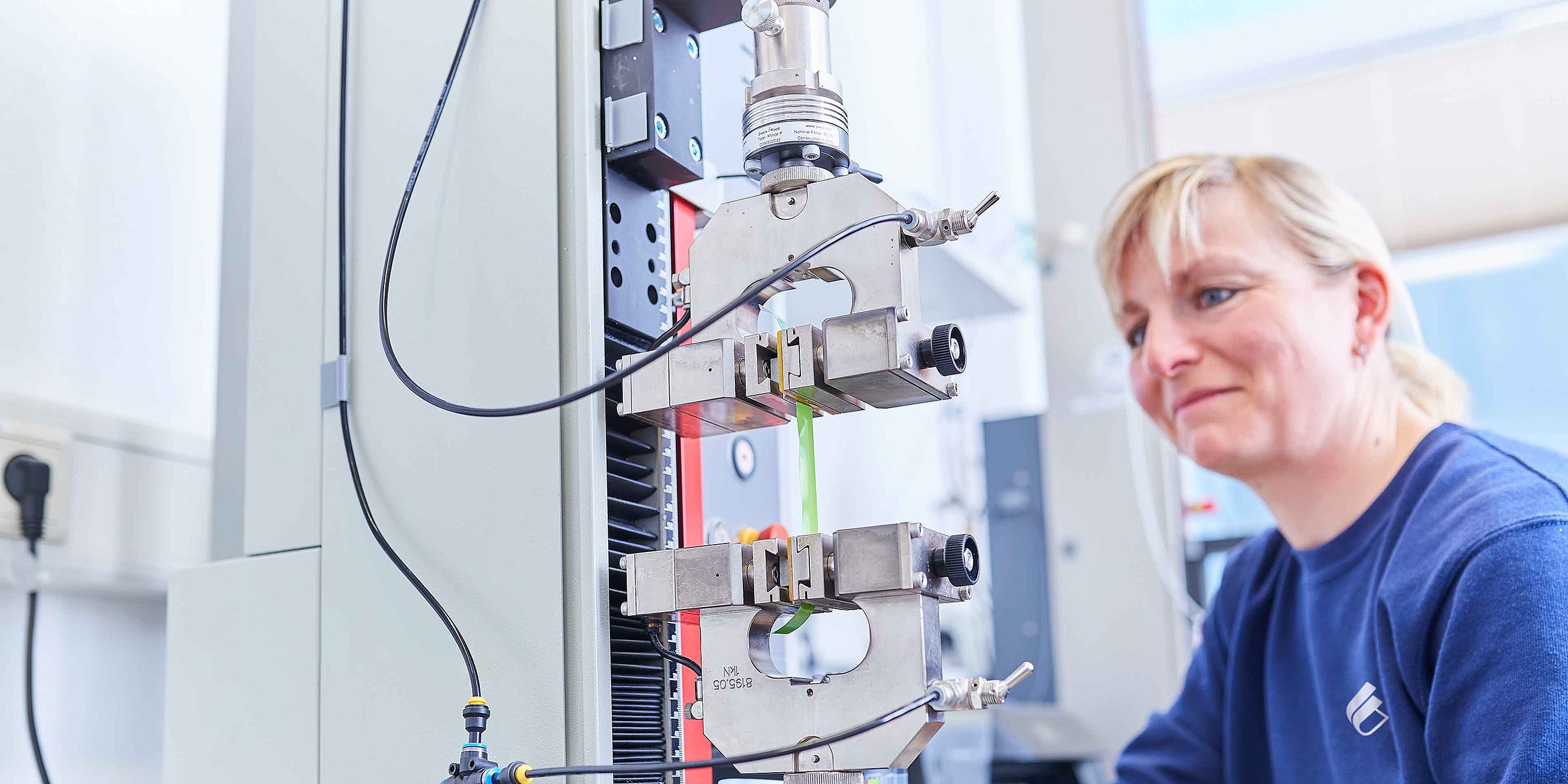 An employee is sat before a microscope in the laboratory and is checking the products for quality and adherence to specifications