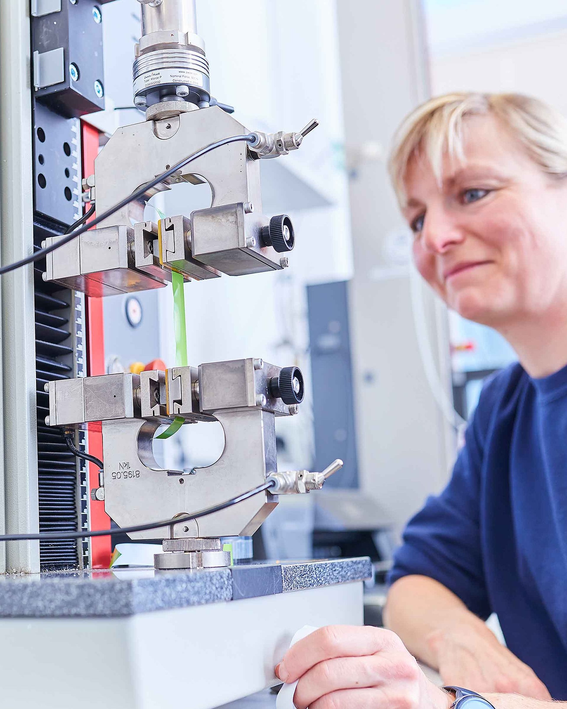 Eine Mitarbeiterin sitzt vor einem Mikroskop im Labor und prüft die Produkte auf ihre Vorgaben und Qualität