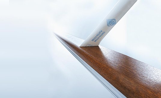 Eine weiße TacFlex® Oberflächenschutzfolien für Fensterprofile wird von einem brauen Fensterrahmen abgezogen