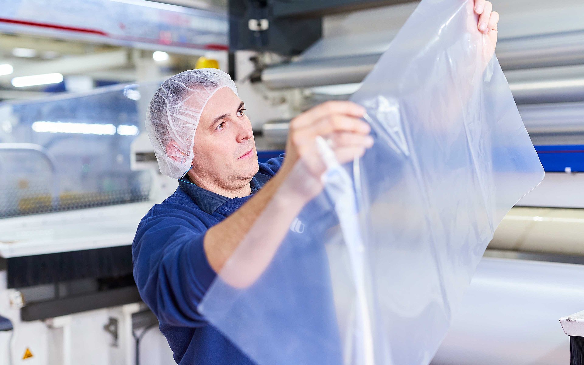 Un collaborateur en vêtement de travail bleu foncé portant une résille tient un film plastique dans sa main.
