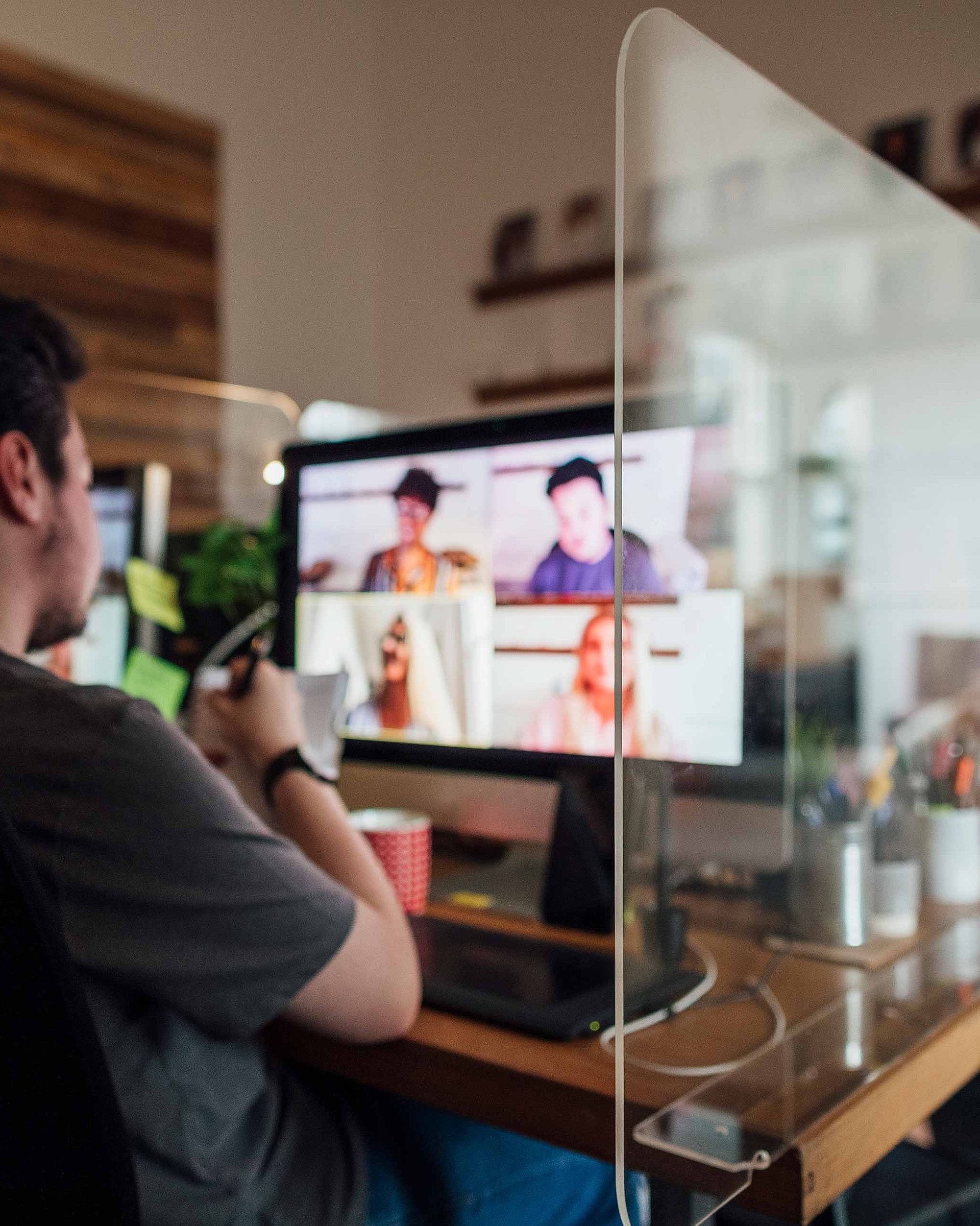 A man is sitting in front of a computer. The picture shows a monitor on which an online meeting is taking place