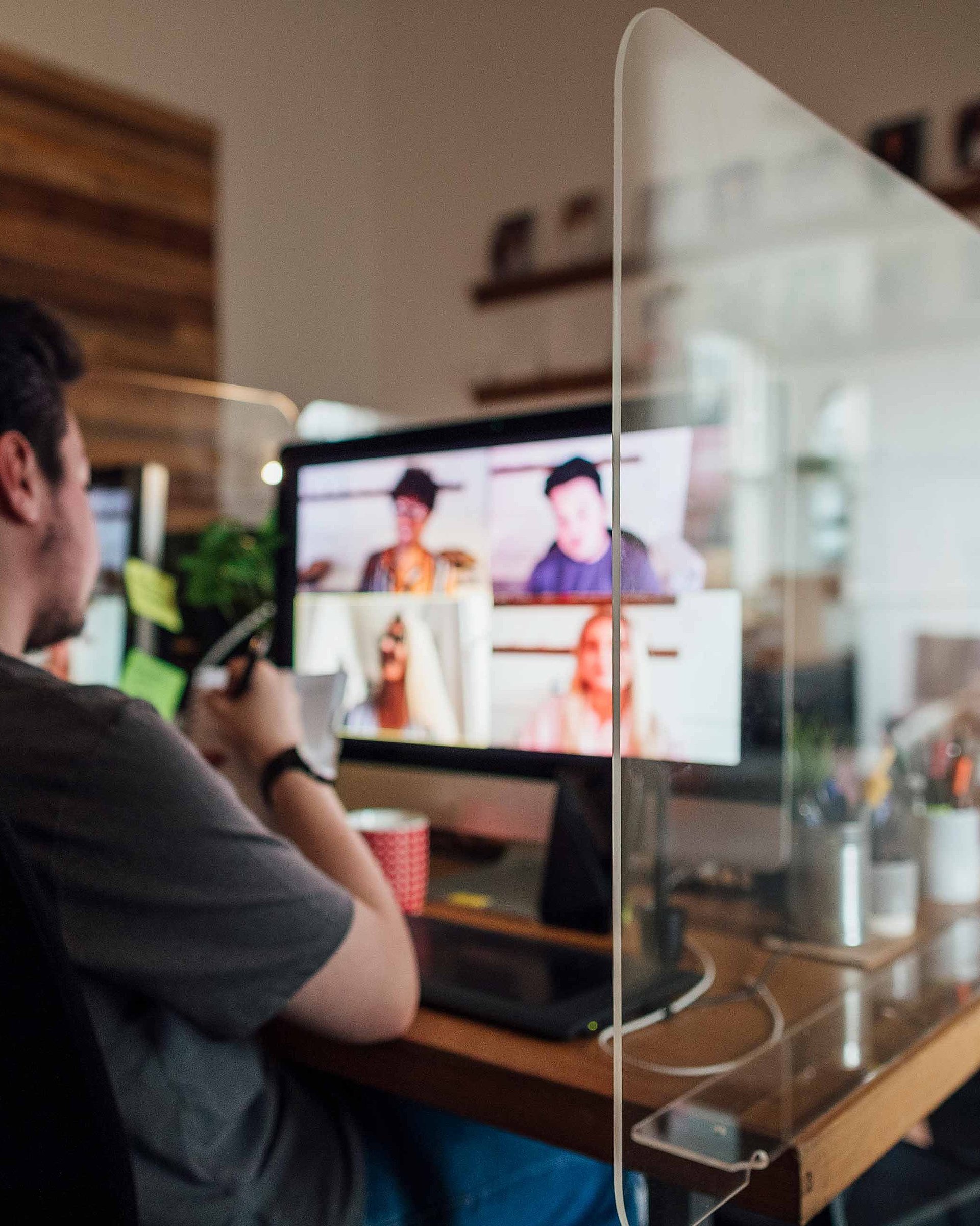 Ein Mann sitzt vor einem Computer. Zu sehen ist ein Bildschirm, auf dem ein Online-Meeting stattfindet