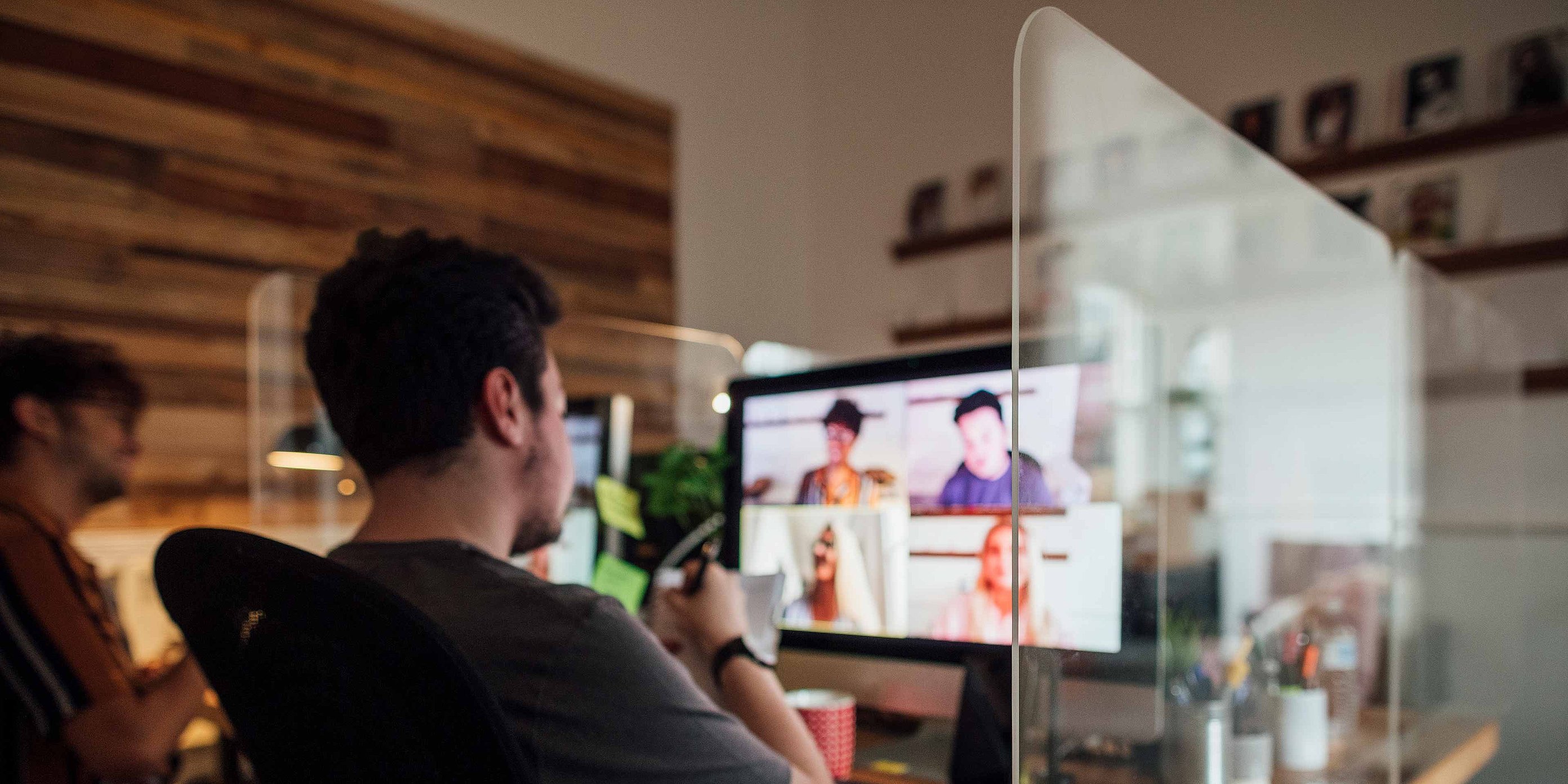 A man is sitting in front of a computer. The picture shows a monitor on which an online meeting is taking place