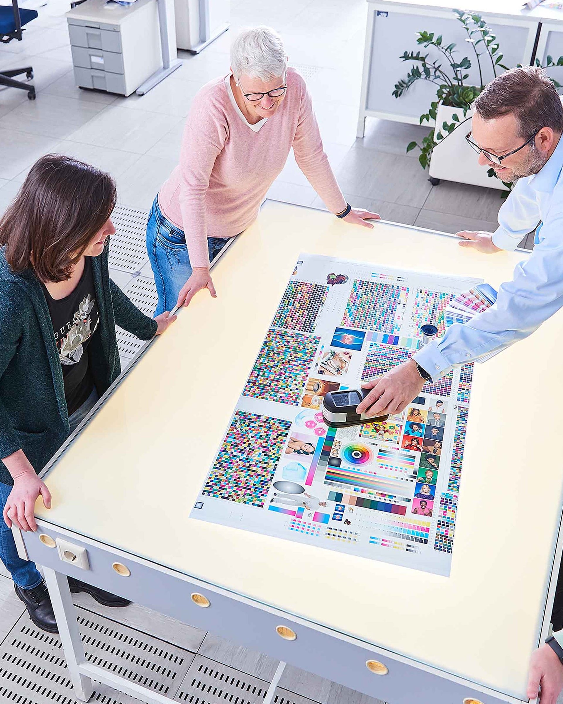Four employees are standing together around a table and discussing a printed sample