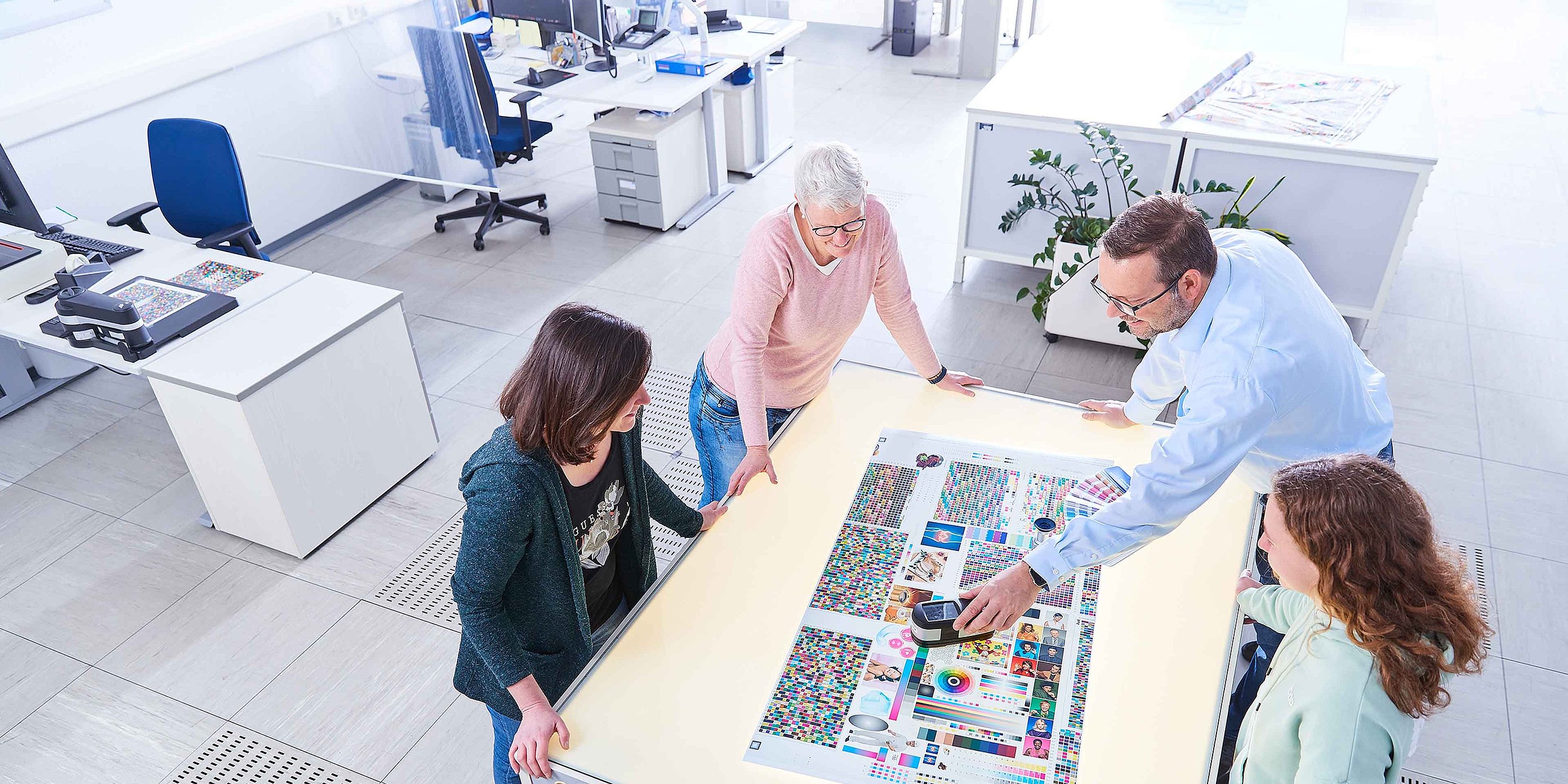 Four employees are standing together around a table and discussing a printed sample