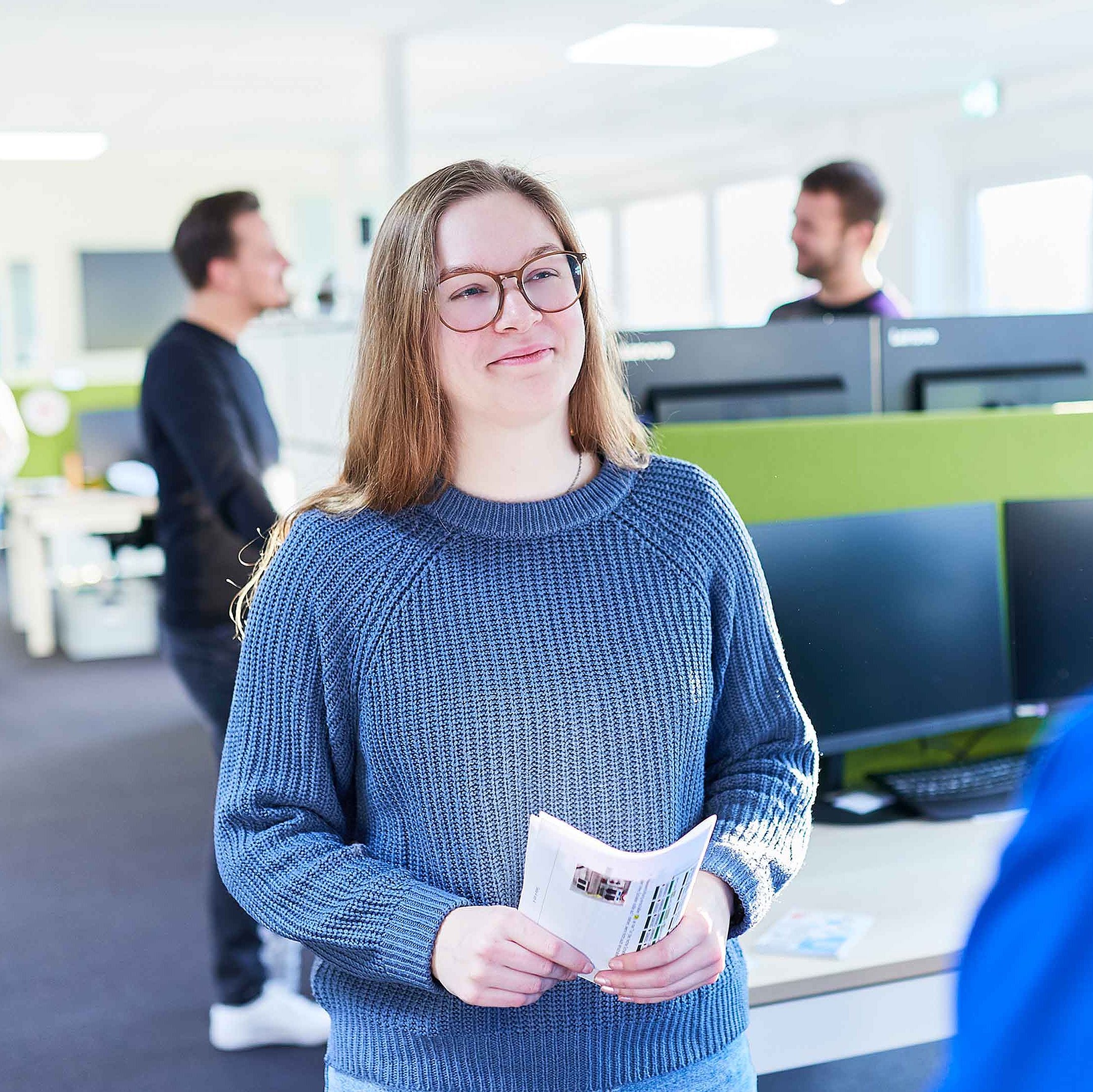 An employee is standing in the office, holding a flyer