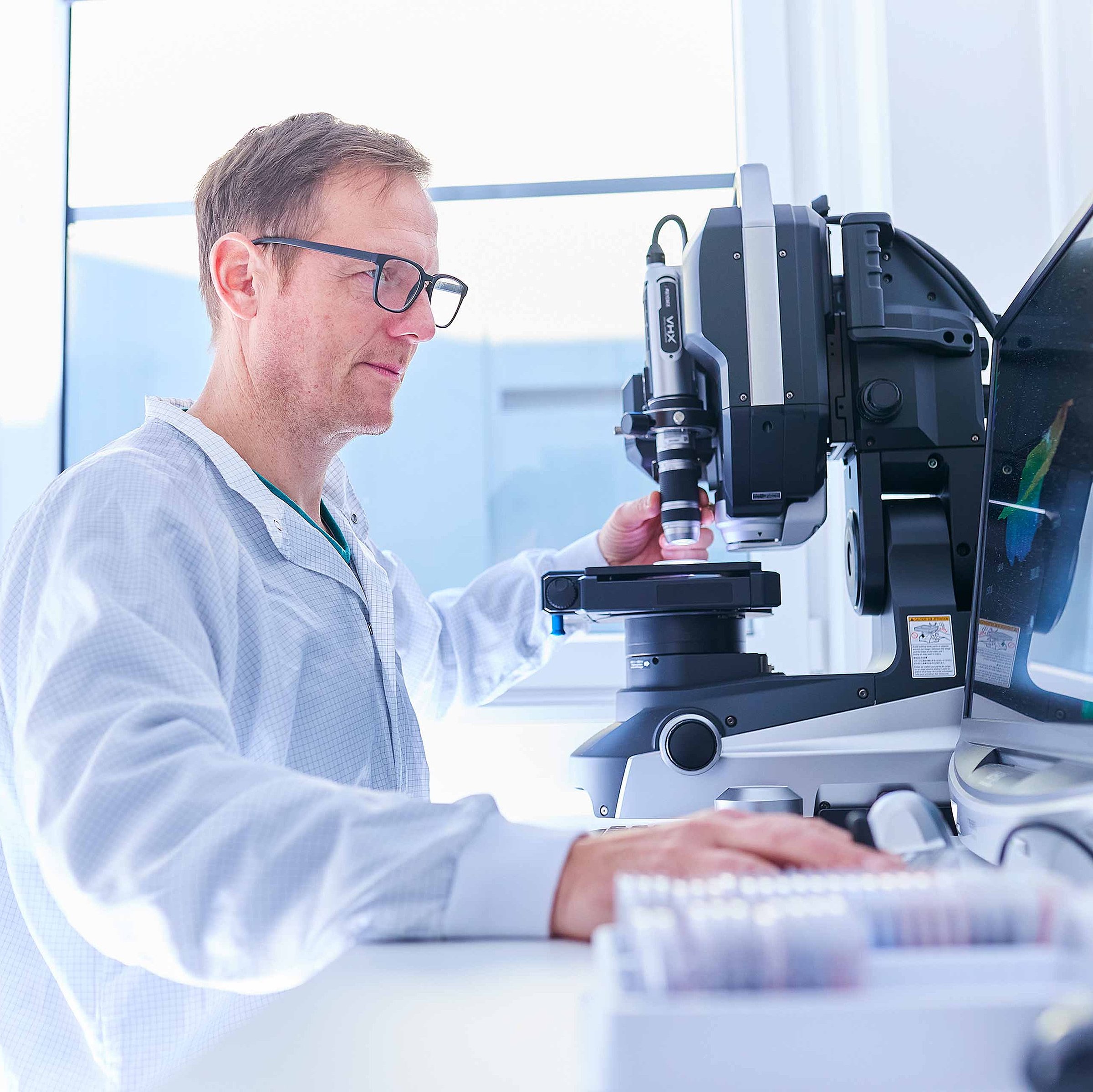 An employee is sat before a microscope in the laboratory and is checking the products for quality and adherence to specifications