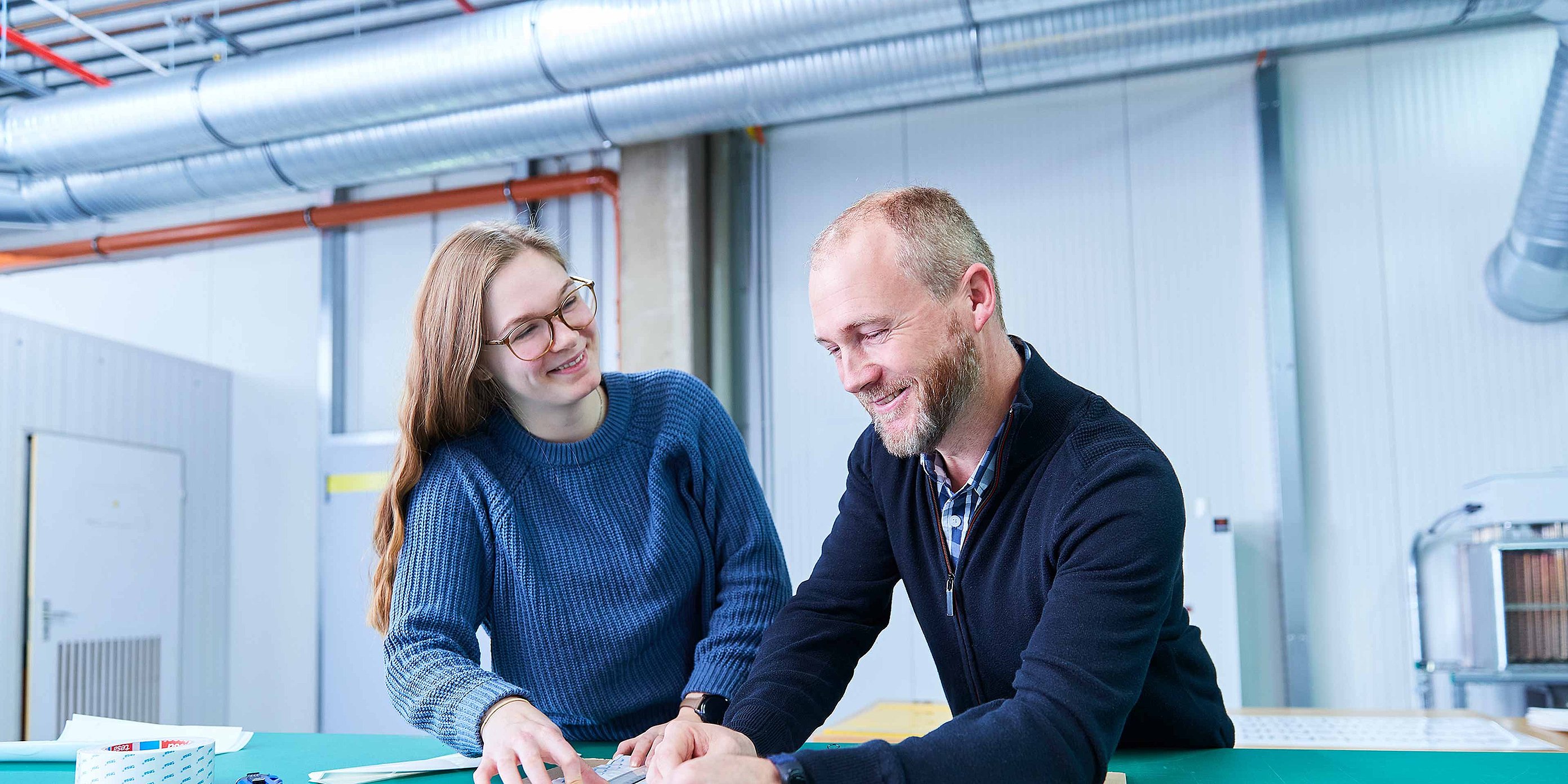 Two employees are standing next to one another discussing technical details
