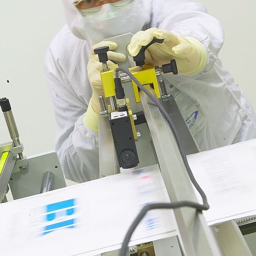 Pracownik w odzieży ochronnej reguluje żółte urządzenie pomiarowe na przenośniku taśmowym w laboratorium cleanroom