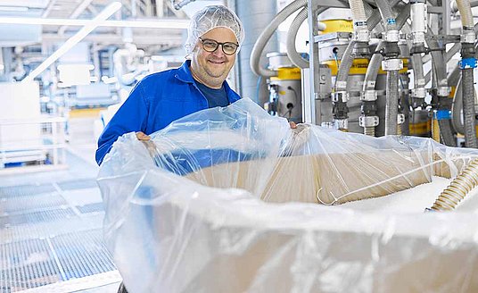 Product photo of the In-Liner; an employee wearing blue work clothes and a hairnet is holding a large transparent plastic sheet