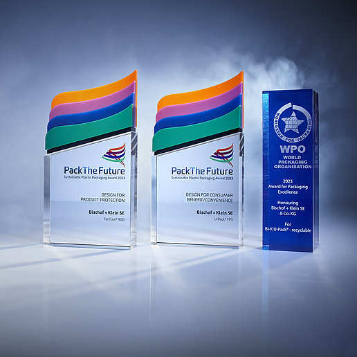 Bild mit drei Awards, die 2023 gewonnen wurden: World Star Packaging Award für den U-Pack® recyclingfähig, Pack The Future Award für den U-Pack® ffs und Pack The Future Award für TacFlex® 900. Die Awards stehen nebeneinander vor einem dunklen Hintergrund und sind beleuchtet.