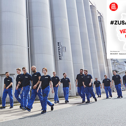 Mehrere Auszubildende in Arbeitskleidung gehen an Silos an der Produktionshalle in Lengerich entlang