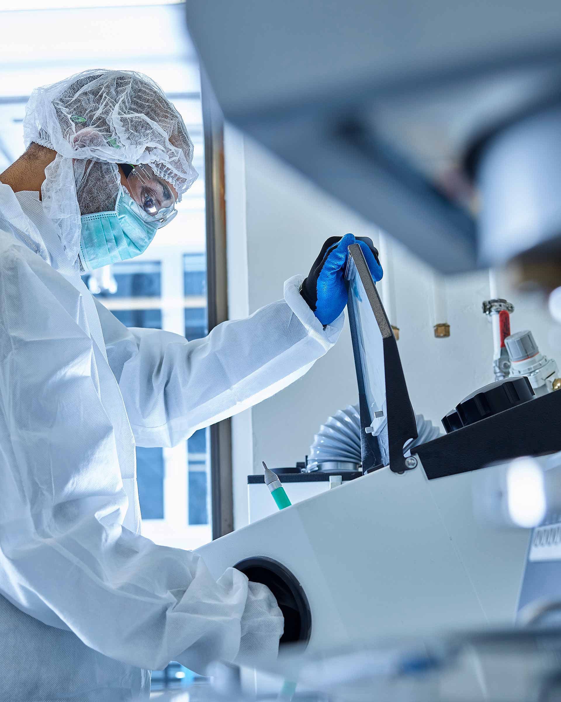 A person in protective clothing is operating laboratory equipment in a laboratory environment
