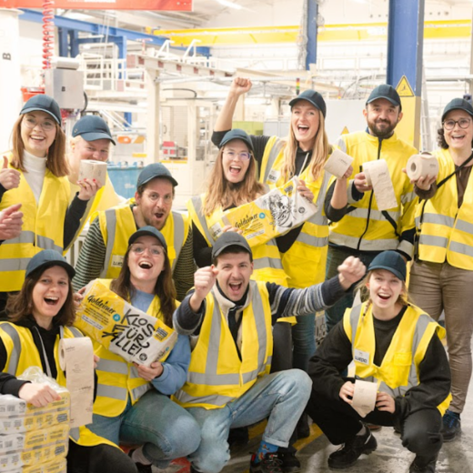 Bischof+Klein Mitarbeiterin zusammen mit Mitarbeitenden von Wildplastic, Goldeimer und Wepa in der Produktionshalle. Sie halten alle einen Toilettenpapierpackung von Goldeimer in der Hand