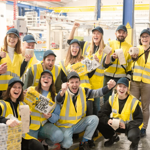 Des collaborateurs de Bischof+Klein avec des collaborateurs de Wildplastic, Goldeimer et Wepa dans le hall de production. Ils tiennent tous un paquet de papier toilette de Goldeimer dans la main