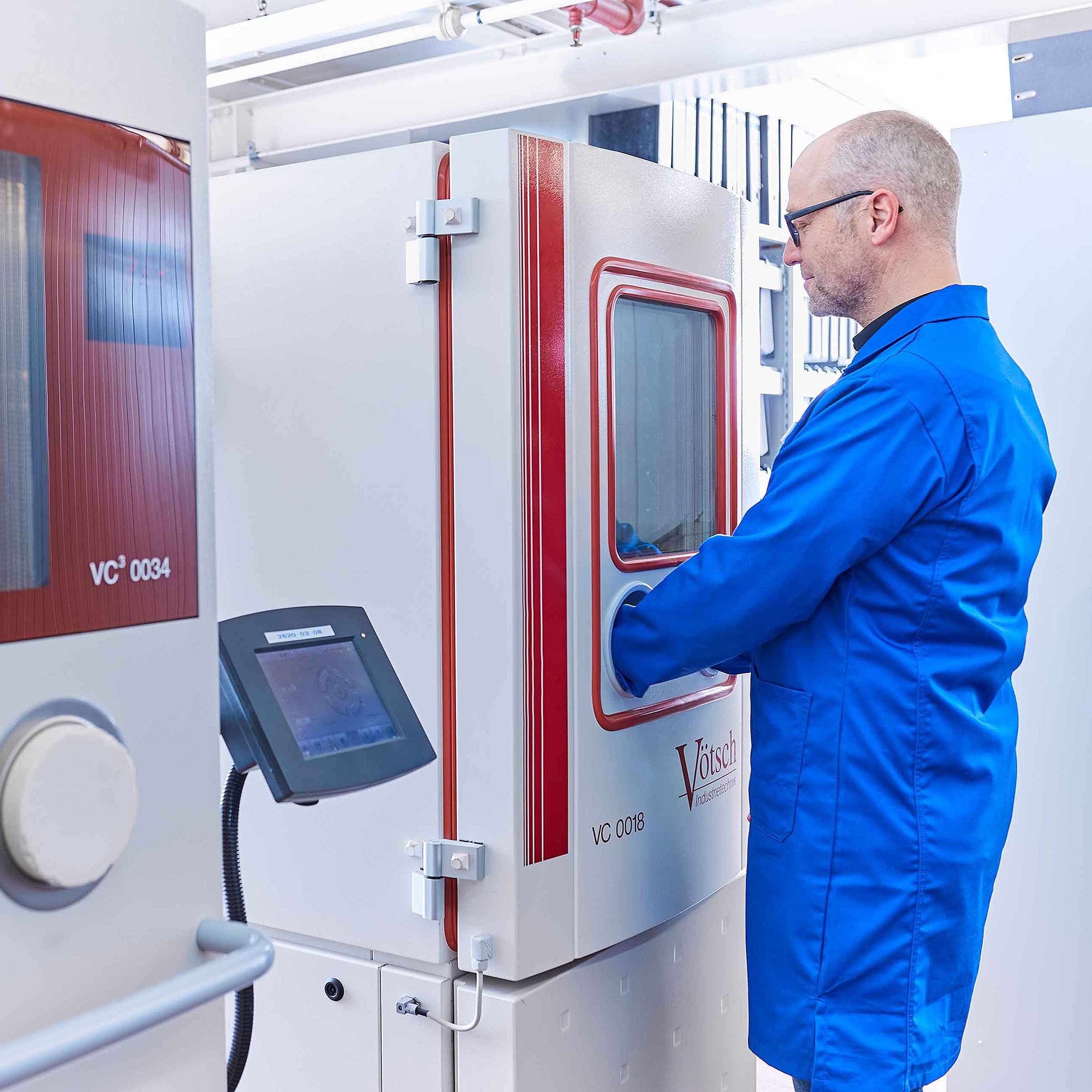 An employee wearing work clothing is standing at a machine that is used to check the quality of manufactured products