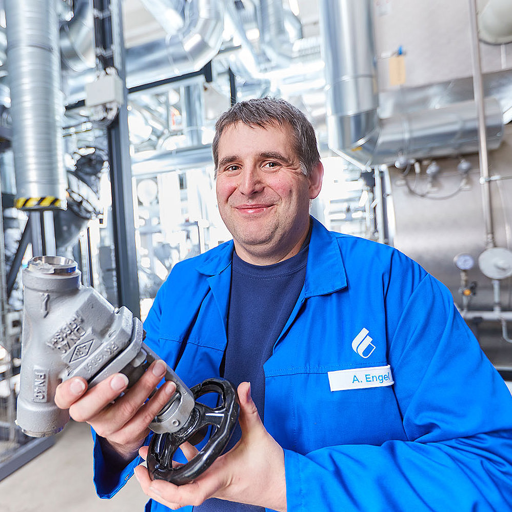 Mitarbeiter in blauer Arbeitskleidung steht an einer Maschine und bedient diese